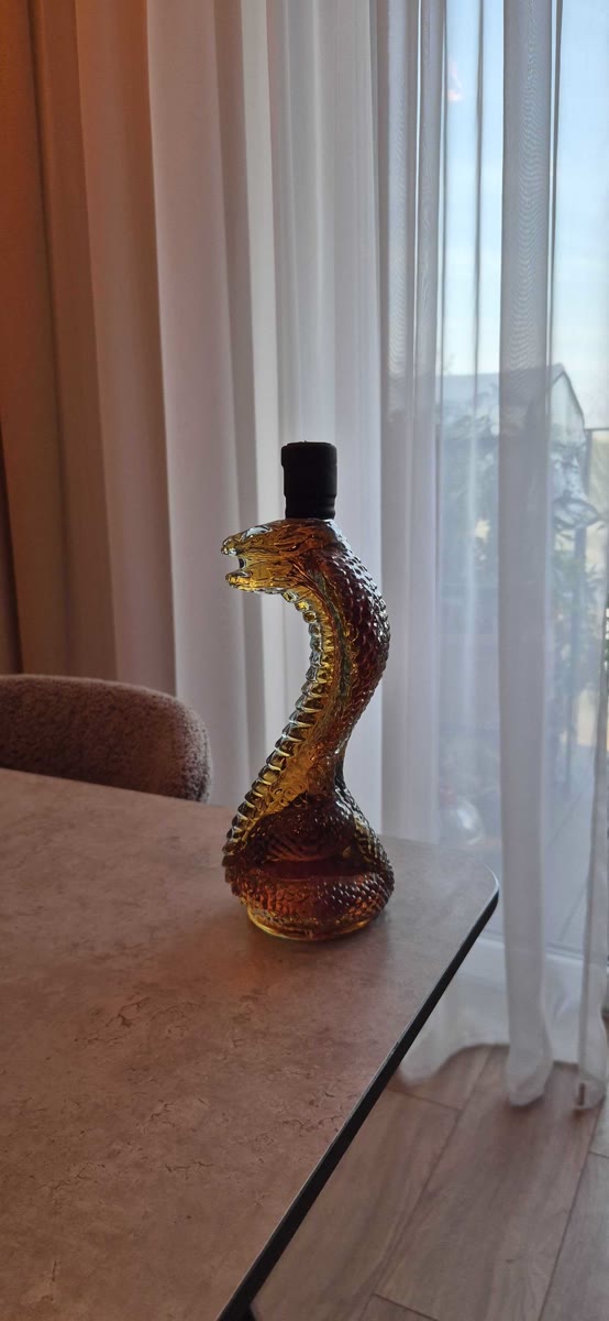 Phone photo of a cobra-shaped glass bottle on a table by a window