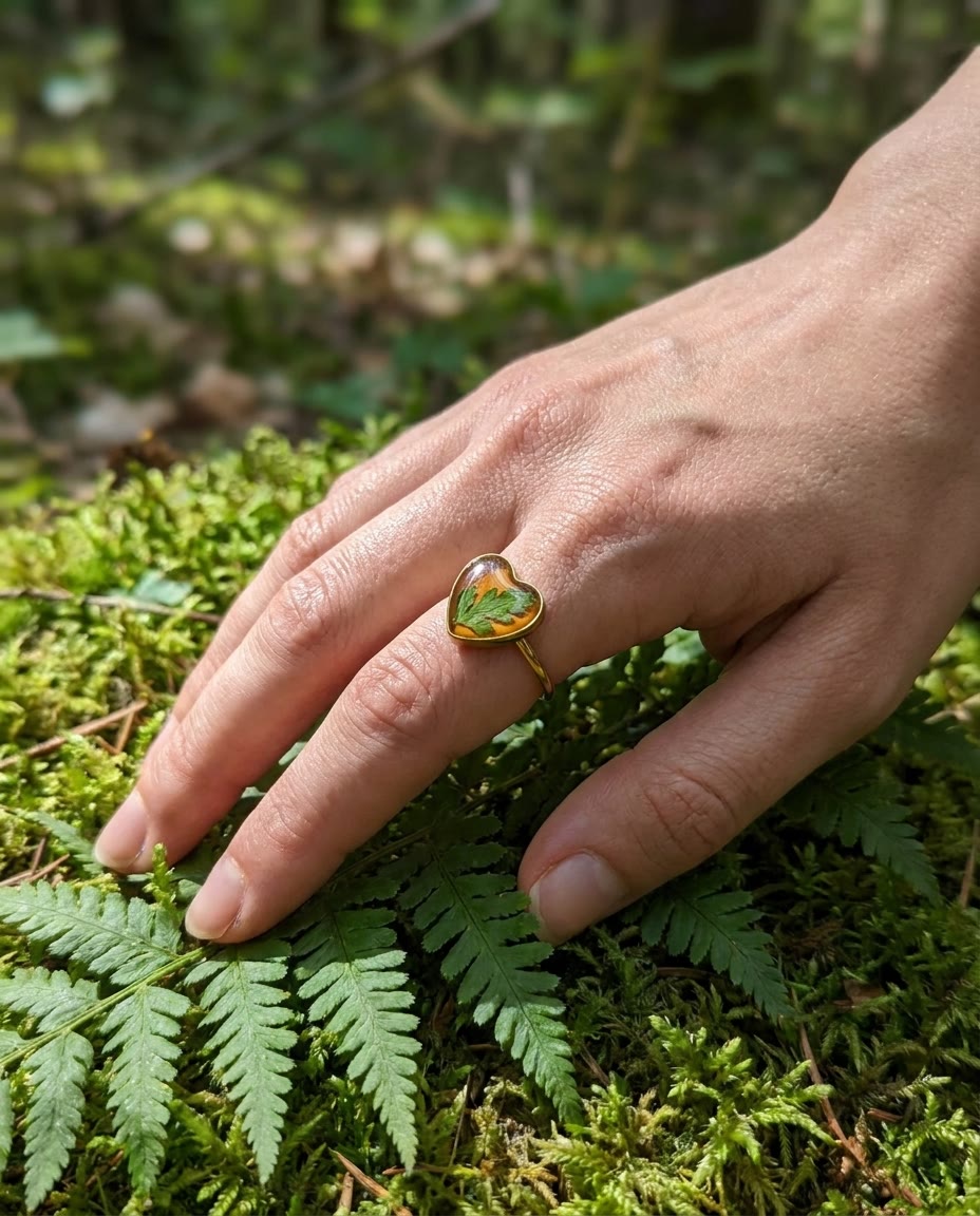 Pressed fern resin ring worn on a hand resting on moss and ferns